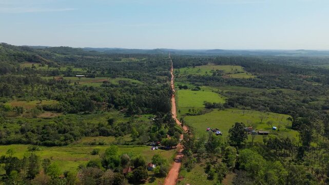 Aerial view of a long dirt road crossing green farmland in Nueva Alborada