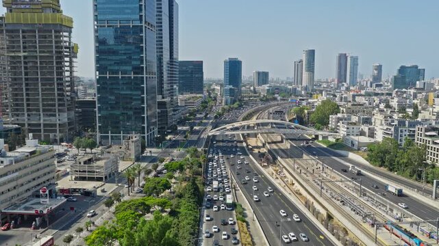 Aerial drone shot flying parallel to Ayalon Highway traffic, train tracks, and modern financial district skyscrapers in Tel Aviv Israel.