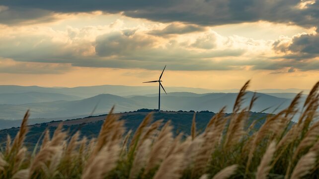 Wind turbines in a scenic countryside landscape with golden grass, mountains and dramatic sunset sky