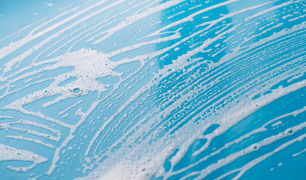 Diagonal cleaning foam streaks across a blue surface with small bubbles.