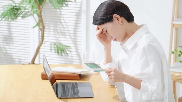 通帳を見て悩む女性。貯金、銀行、心配、不安、疑問、ローン、悩み、資金、困る、老後、貯蓄、不満、支払い