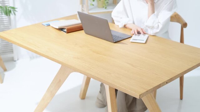 A middle-aged woman ponders while looking at her laptop. Household finances, accounting, administrative tasks, anxiety, worries, dissatisfaction, questions, management, calculator, DX.