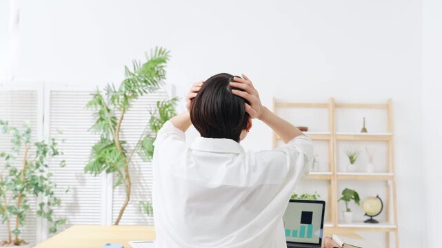 オフィスで頭を抱える女性の後ろ姿。困る、失敗、不満、不安、心配、オフィス、カジュアル、悩み、問題