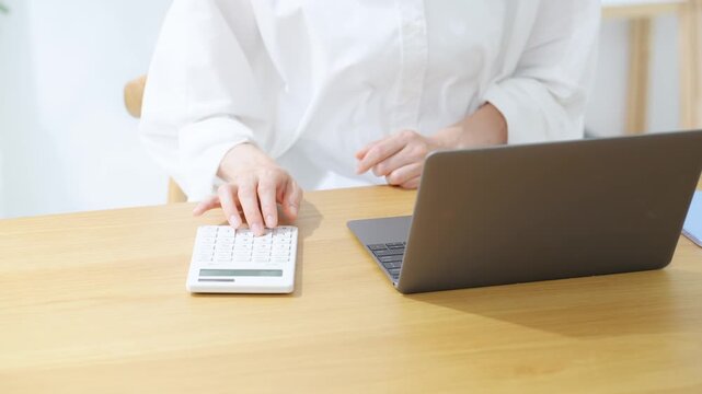A woman using a laptop and calculator. Household finances, bookkeeping, accounting, calculations, finance, estimation, freelance, qualifications.
