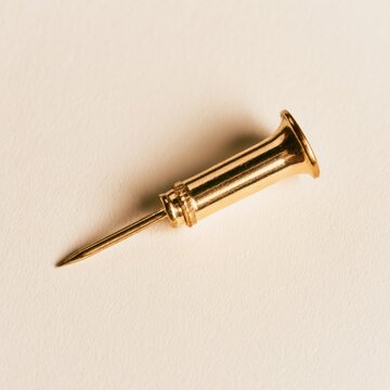 Golden needle with a flared end close up macro shot on a pale background