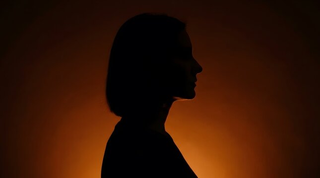 Dramatic silhouette profile of woman against warm orange background