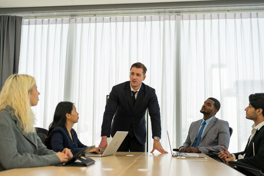 Business manager leaning on table talking to team in office meeting