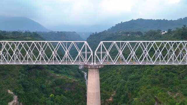 Aerial view of a massive steel truss railway bridge spanning a deep, lush green mountain valley.