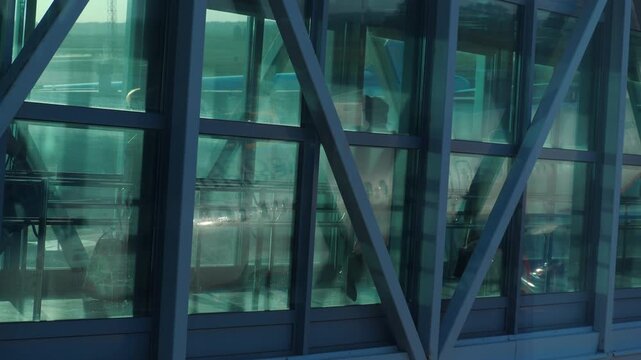 Passengers with luggage walk through glass jet bridge toward airplane at airport gate, aircraft reflections in windows, soft evening light, static side view