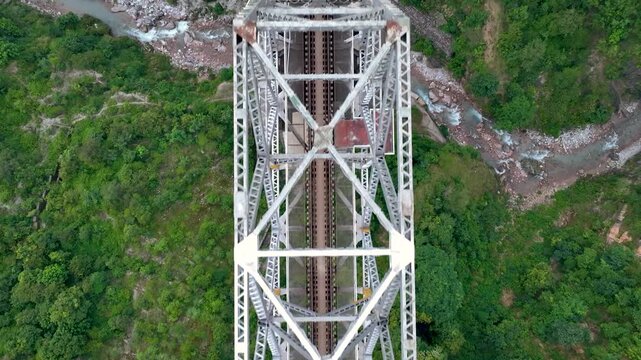 Birds eye Aerial view of a massive steel truss railway bridge spanning a deep, lush green mountain valley.
