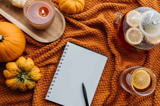 Autumn hygge concept with notebook, tea, pumpkins, and candles