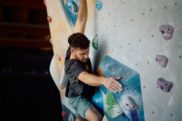 Young athlete exercising wall climbing in bouldering center. © Drazen