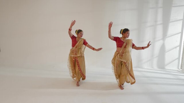 Two women are performing a traditional Indian dance in a bright studio setting