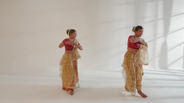 Two women are performing Indian classical dance steps in a studio setting