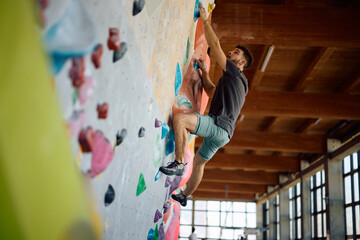 Obraz premium Below view of athlete practicing climbing technique on bouldering wall.