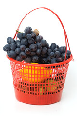 Obraz premium Red basket holds dark grapes and yellow lemons. Fresh fruit displayed in simple, vibrant container. Bright red basket contrasts with white background
