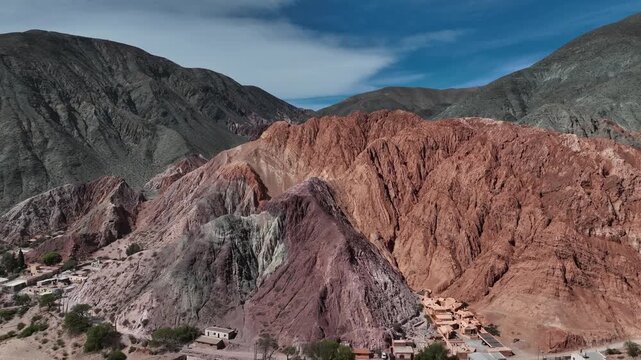 A smooth drone flight over the Hill of Seven Colors in Purmamarca, Jujuy. The mountain range in the background creates a stunning contrast. Traditional houses appear at the base of the hill.