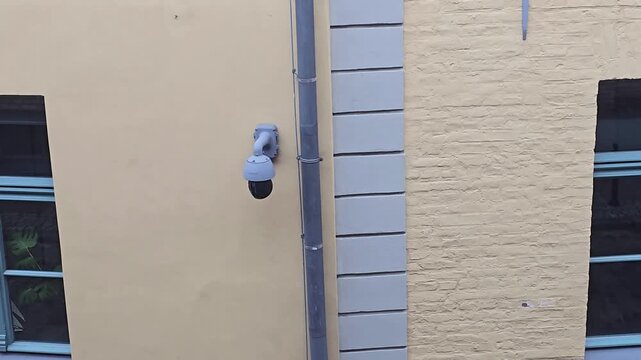 Surveillance camera slowly rotates above urban street facade in Gdansk Poland