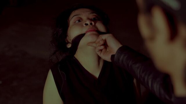 A close-up of a hostile man holding a terrified, gagged woman by the chin, forcing eye contact. Cinematic portrayal of a kidnapping or hostage situation.