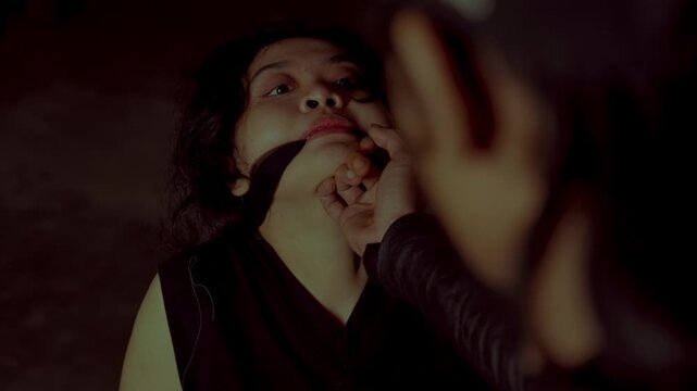 A kidnapper violently holds the jaw of a crying, gagged female victim. A powerful, dark cinematic shot representing domestic abuse or human trafficking.