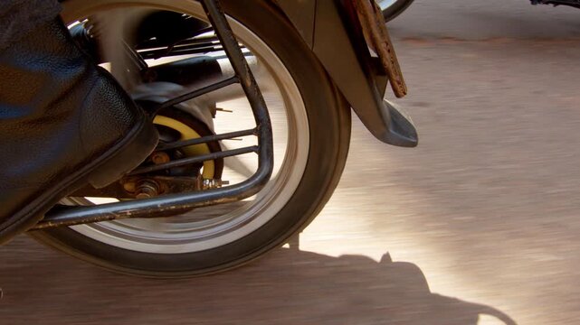 Motorcycle wheel of a boda boda taxi moving through Kampala, with tire, spokes, chrome components and road surface visible in close detail, street-level moving shot