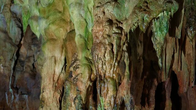 Close-up view of colorful stalactites and stalagmites inside Aggitis Cave, showing green, brown, and beige mineral deposits on rock formations. Static locked shot capturing the textured limestone.