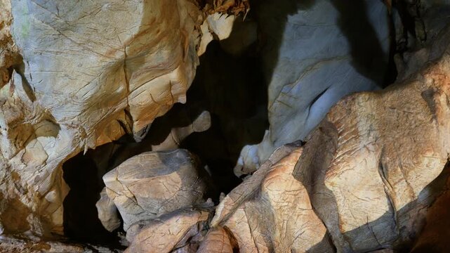 Illuminated limestone rock formations inside a natural cave system reveal layered geological structures and deep shadows. Smooth overhead tracking shot showcases the textured ceiling and walls.