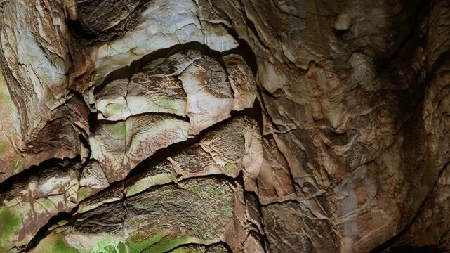 Layered limestone rock formations display textured surfaces with natural mineral deposits inside an underground cave. Static close-up shot captures geological detail with subtle ambient lighting.