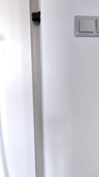 A hand takes a shoehorn from a wall hook beside a white entrance door, practical home organization, daily routine, hallway storage.