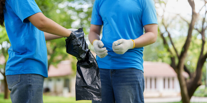 Volunteers holding black garbage bag during outdoor environmental park cleanup