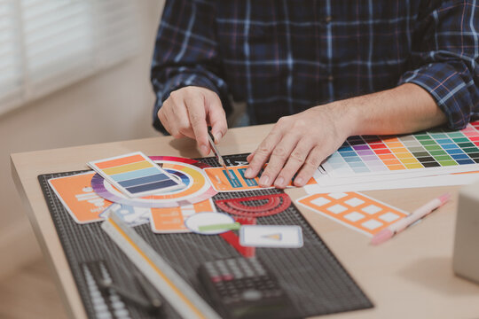 Designer working with color palettes, layout templates, and creative design tools on a desk while planning branding and graphic design projects in a modern office.
