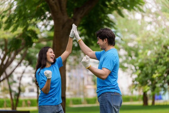 Asian volunteers high five after successful environmental cleanup in park