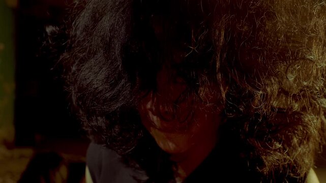 Intimate and chilling portrait of a captive woman looking down, her face obscured by wild, unkempt hair. Warm, dramatic lighting highlights the gritty reality of her captivity.