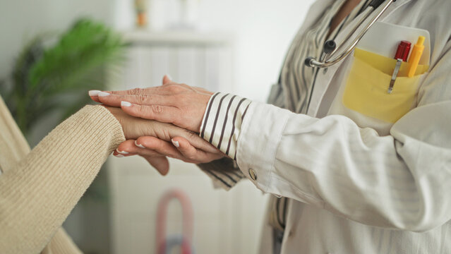 Woman doctor holds patient's hands and touches wrist with visible stethoscope, comforting in clinic building; compassion care trust.
