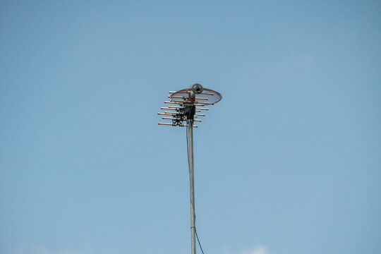 Outdoor television antenna mounted on a tall metal pole against a clear blue sky. It features horizontal metal dipole elements to capture signals.