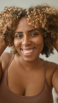 Woman smiling, hands to face wearing a soft thin tank top in a studio setting; warm joy self acceptance.