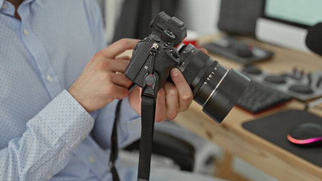 Man in light blue shirt points finger to camera dial while holding mirrorless lens in studio; concentrated practice.