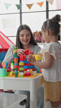 Woman and little girl stacking colorful plastic blocks at a play table in a classroom building; nurturing joy.