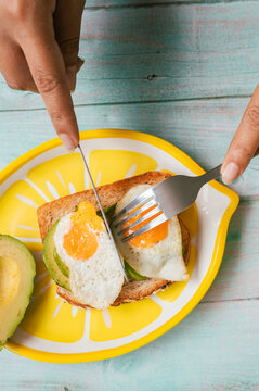 Hands eating avocado toast with fried quail eggs for breakfast
