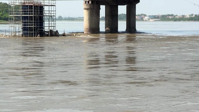 Rushing muddy river water flowing under bridge construction 4k video footage