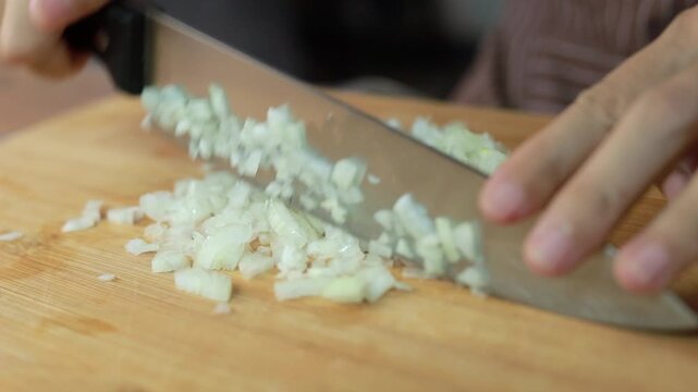 Hands mincing fresh white onion on a wooden cutting board