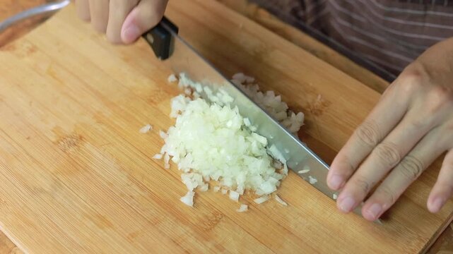 Hands mincing fresh white onion on a wooden cutting board