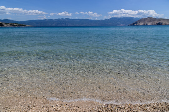 Crystal clear turquoise shallows over pebbles at Ba&scaron;ka beach with the Velebit mountains across the channel, Krk island, Croatia