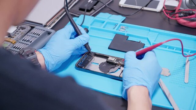technician repairing internal micro-electronics component inside an opened smartphone on a blue mat as a concept for hardware maintenance service, right to repair information technology