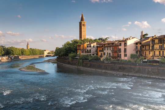 Cityscape of old city on river bank with sunlit roofs and bell tower on sunny day, Verona, Italy