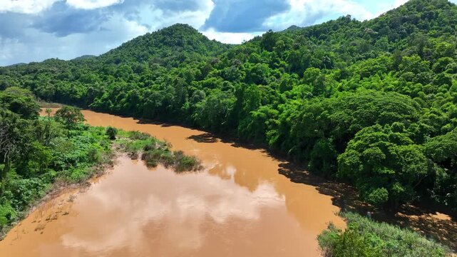 Drone perspective captures floodwater flowing through a tropical rainforest, highlighting heavy rainfall, climate instability, sediment runoff and environmental change. Phrae Province, Thailand. 4k.
