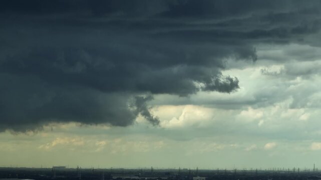 Dramatic cumulonimbus storm clouds loom above the distant landscape, illustrating extreme weather, heavy rainfall risk, atmospheric turbulence and growing climate related challenges. 4k.
