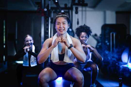 Women's strength and empowerment: a strong Asian athlete loosening up for the session in a dimly lit gym, bonding after training, captured in a cinematic fitness portrait