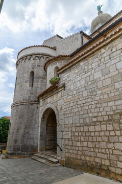 Romanesque apse with blind arcade and side portal of Krk Cathedral below the onion domed bell tower with angel, Krk island, Croatia