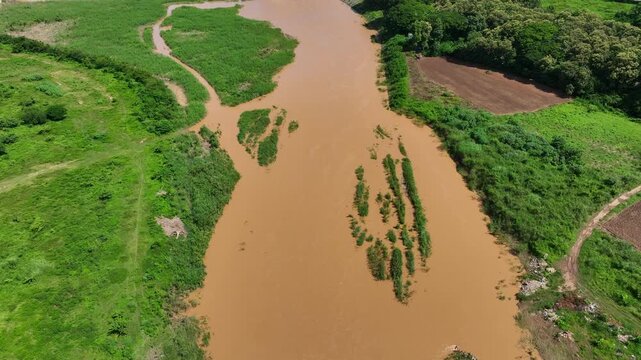 Powerful brown floodwater flows through a rural landscape, illustrating sediment runoff, river overflow, extreme weather, global warming and growing environmental challenges. Phrae Province, Thailand.